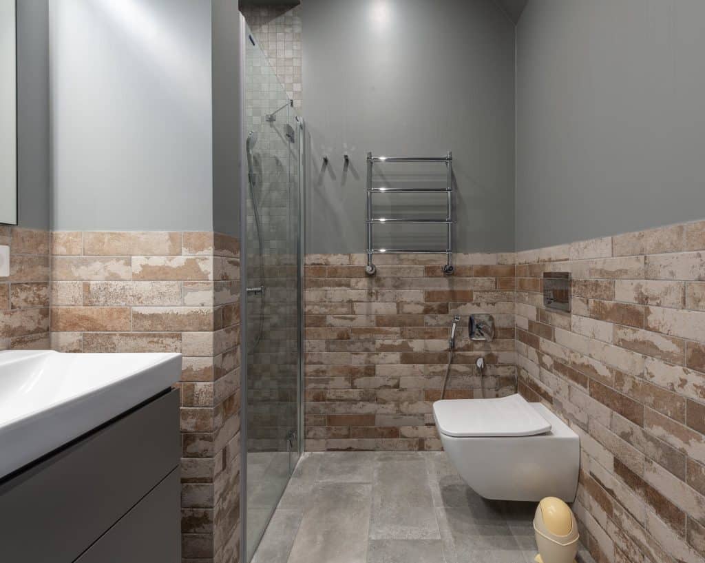 bathroom with shower and toilet with stone coloured tiles and grey wall