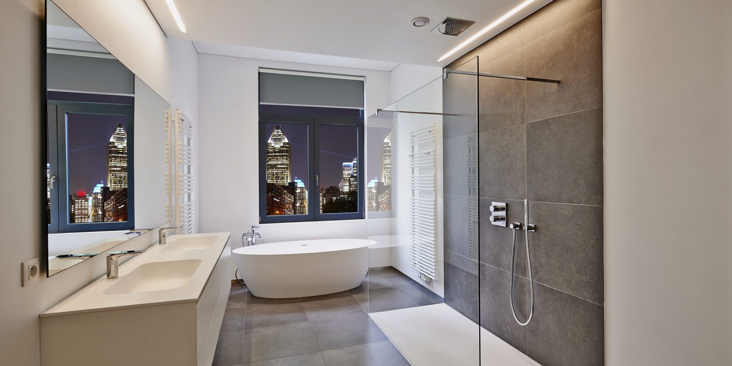 Bathtub in corian, Faucet and shower in tiled bathroom with windows towards night city lights